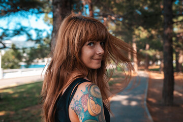 Close up portrait of a young happy woman with a tattoo on her arm is walking in the park and look around. Summertime