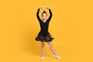 Wall Mural - Cute little girl in black dress dancing on yellow background