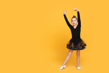 Wall Mural - Cute little girl in black dress dancing on yellow background. Space for text