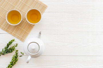 Tea drinking with white teapot and two cups with green leaves, top view