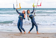 Cheerful Friends Gesturing And Kitesurfing At Beach