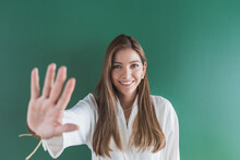 Smiling Woman Showing Stop Hand Sign Against Green Background