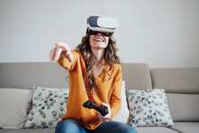 Woman With Joystick Gesturing Wearing Virtual Reality Headset At Home