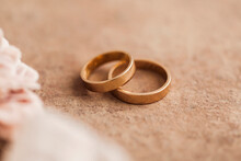 Studio Shot Of Pair Of Golden Wedding Rings Lying Against Brown Background