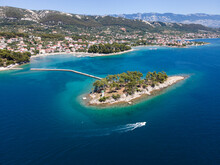 Croatia, Primorje-Gorski Kotar County, Rab, Drone View Of Motorboat Passing Small Coastal Islet With Town In Background