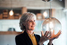 Smiling Businesswoman Looking At Illuminated Pendant Light In Office