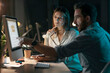 © Westend61 - Thoughtful businesswoman by colleague explaining strategy over computer at night in office