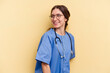 Young nurse caucasian woman isolated on yellow background looks aside smiling, cheerful and pleasant.