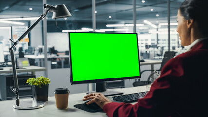 Leinwandbilder - Successful Caucasian Businesswoman Sitting at Desk Working on Green Screen Laptop Computer in Office. Beautiful Businessperson using Chroma Key Display. Over the Shoulder Shot