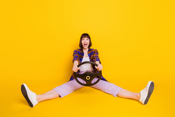 Wall Mural - Portrait of pretty cheerful funky girl sitting holding steering wheel isolated over bright yellow color background