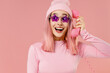 © ViDi Studio - Young fun woman with bright dyed rose hair in rosy top shirt hat glasses hold handset vintage phone look aside isolated on plain light pastel pink background studio. People lifestyle fashion concept.