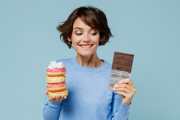 Wall Mural - Young wistful happy woman 20s in casual sweater hold sweet pink cream donuts chocolate bar look camera isolated on plain pastel light blue background studio portrait. People lifestyle food concept