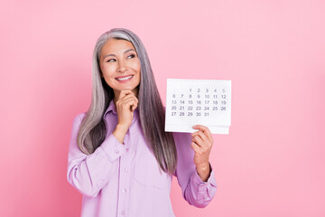 Portrait of attractive minded cheerful gray-haired woman holding calendar thinking isolated over pink pastel color background