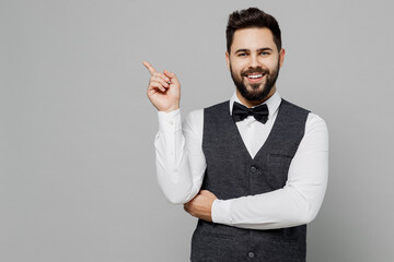 Wall Mural - Young barista male waiter butler man 20s wear white shirt vest elegant uniform work at cafe point index finger aside on workspace isolated on plain grey background studio. Restaurant employee concept.