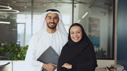 Wall Mural - Man and woman with traditional clothes working in a business office of Dubai. Portraits of  successful entrepreneurs businessman and businesswoman in formal emirates outfits. Concept about middle east