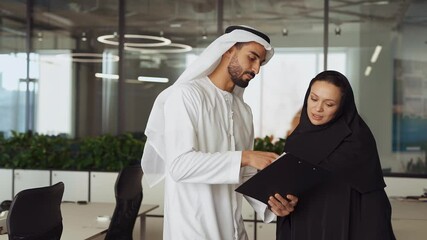 Wall Mural - Man and woman with traditional clothes working in a business office of Dubai. Portraits of  successful entrepreneurs businessman and businesswoman in formal emirates outfits. Concept about middle east