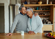 Happily retired elderly biracial couple holding each other lovingly in modern kitchen. 