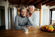 Portrait of happily retired elderly biracial couple leaning on kitchen counter, smiling at camera. Healthy lifestyle in modern kitchen.