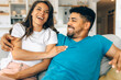 © Astarot - A young mixed-race couple is sitting together at home, cuddling and hugging.