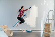 Repair concept. Funny smiling lady holding paint roller, jumping and flying at her room while renovating her apartments