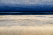 Surging Waves And Grey Steely Skies Spill Onto The Beach During The Twilight Hours.