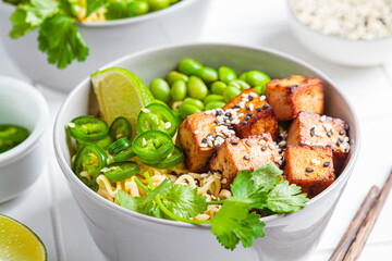 Wall Mural - Vegan noodles ramen soup with marinated tofu, edamame beans and hot peppers in gray bowls.