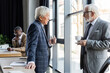 © LIGHTFIELD STUDIOS - interracial businessmen talking in office near blurred african american colleague