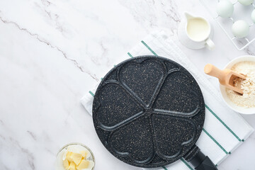 Empty frying pan black, skillet with stone nonstick coating for baking pancakes in shape of breakfast hearts and ingredients on gray concrete table background. Breakfast for Valentines Day. Top view.