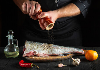 The chef prepares fresh fish sprinkling pepper. Preparing to cook fish food. Working environment in the restaurant or cafe kitchen.