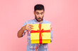 Portrait of curious happy man opening gift, peeking inside box with nosy look, unpacking present, in anticipation of interesting birthday surprise. Indoor studio shot isolated on pink background.