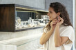 Young pretty female buyer in white pullover trying on new earrings in large modern luxurious jewelry shop