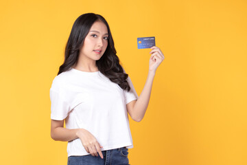 Wall Mural - Portrait of a happy young asian woman wearing white shirt holding bank card, credit card isolated on yellow background. Business online shopping concept.