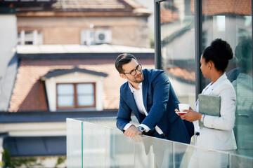 Business coworkers talk while drinking coffee on balcony at work.