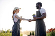 © Roman - Handshaking between farmers and customers for business partners. Farmer working in hydroponic vegetable garden at greenhouse. Successful work of black man and redhead caucasian female in uniform