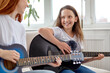 © Roman - Learning to play the guitar. Nice Female teacher explains to child the basics of playing guitar in bright cozy room, at home. Individual home schooling or extracurricular lessons. Side view portrait