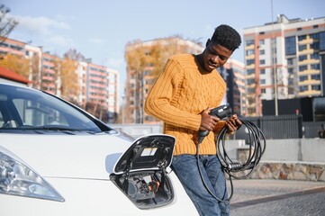 Wall Mural - African American man charging his electric car.