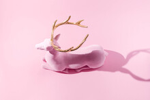 A Pink Reindeer With Golden Horns  On Pastel Pink Background. Minimal Winter Festive Season Creative Concept For Web Banner Or Card. Surreal Traditional Christmas Or New Year Symbolic Design.