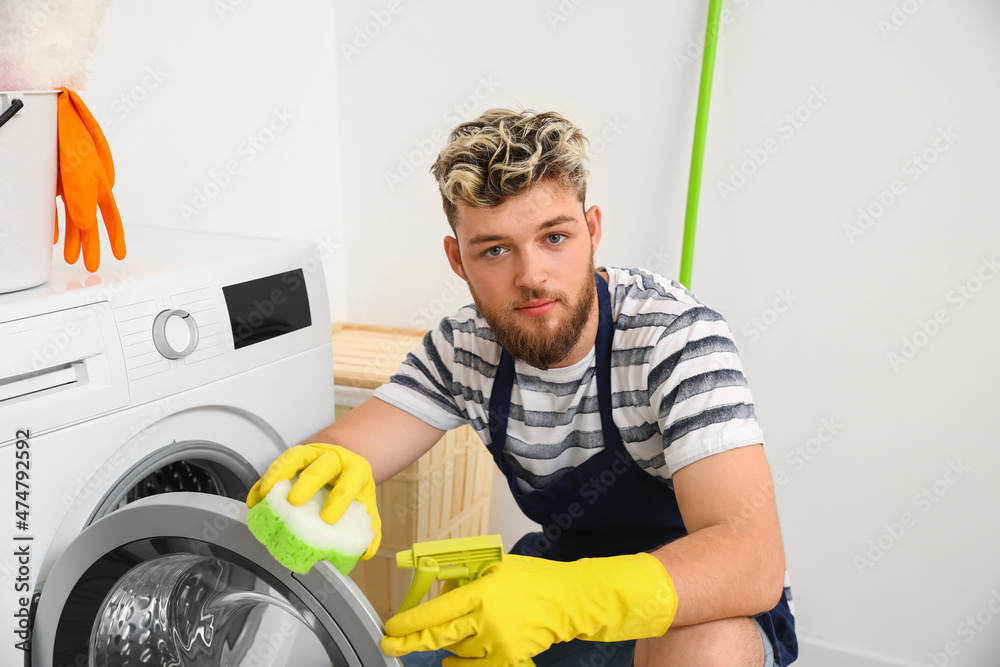 Handsome young man with sponge cleaning washing machine in bathroom