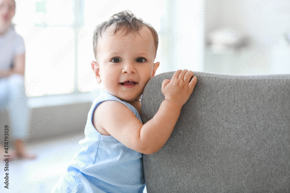 Little baby boy learning to walk near sofa at home