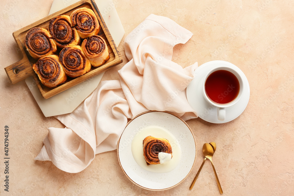 Wooden board and plate with tasty cinnamon rolls on beige background