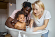© Roman - joyful black and caucasian parents washing daughter child girl in small bathtub, playing with soap and foam, at home, have fun together, laughing. clean skin, skincare, childhood, lifestyle concept
