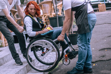 Wall Mural - Waiters lift a girl in a wheelchair up the steps without a ramp. A woman is going to have lunch in a cafe inaccessible to people with special needs