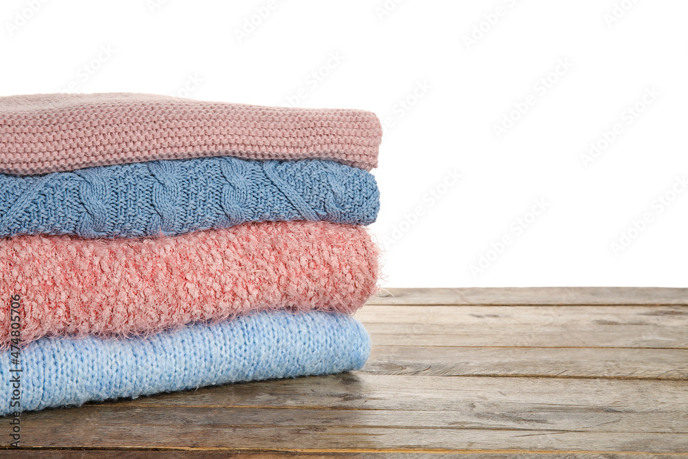 Stack of trendy warm sweaters on wooden table against white background, closeup