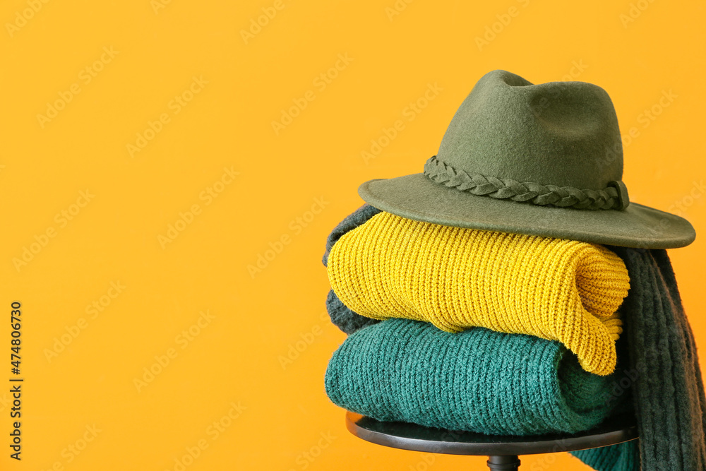 Stylish winter clothes on stool against color background