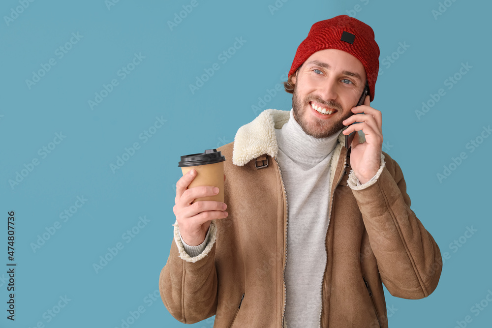 Handsome man with coffee talking by mobile phone on color background