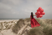 Woman In Red Dress Holding Bunch Of Balloons On The Beach In The Dunes