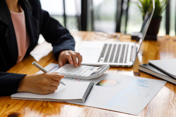 Wall Mural - Close up a Business woman using calculator and laptop for doing math finance on a wooden desk, tax, accounting, statistics, and analytical research concept