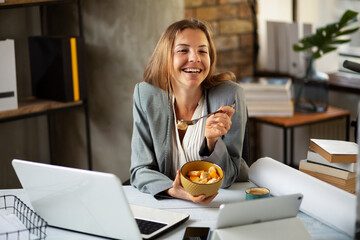 Businesswoman in office having healthy snack. Young woman eating fruit while having a video call.