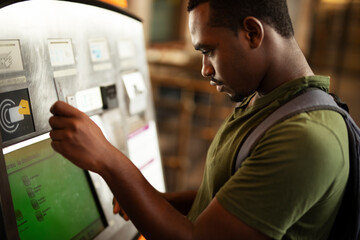 Wall Mural - Smiling African man using ATM machine. Happy young  man withdrawing money from credit card at ATM