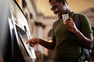 Wall Mural - Smiling African man using ATM machine. Happy young  man withdrawing money from credit card at ATM